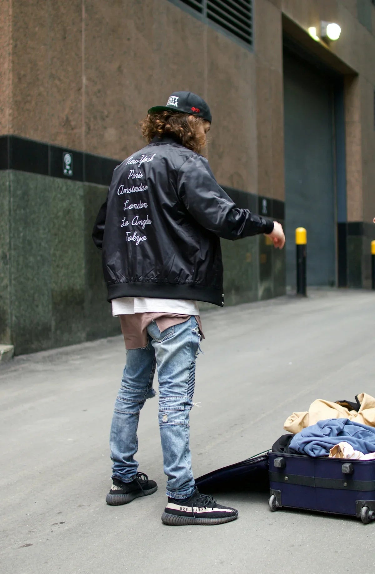 Ung man med streetwear, keps och jeans vid resväska, urban miljö, nördiga kläder
