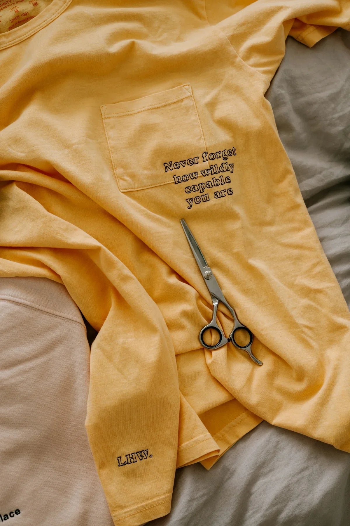 Gul t-shirt med tryck 'Never forget how wildly capable you are', sax bredvid på sängen, Nerdbutiken