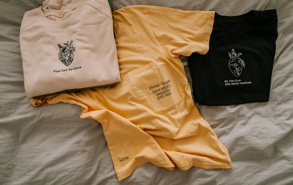 Tre t-shirts med inspirerande text och hjärtmotiv från Nerdbutiken på säng, geek-prylar