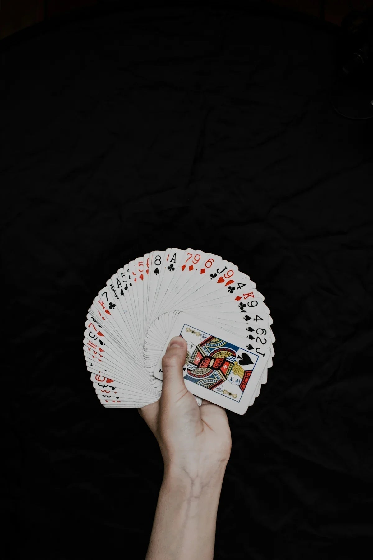 Hand håller solfjädrad kortlek mot svart bakgrund, Nerdbutiken nördiga spelprylar.