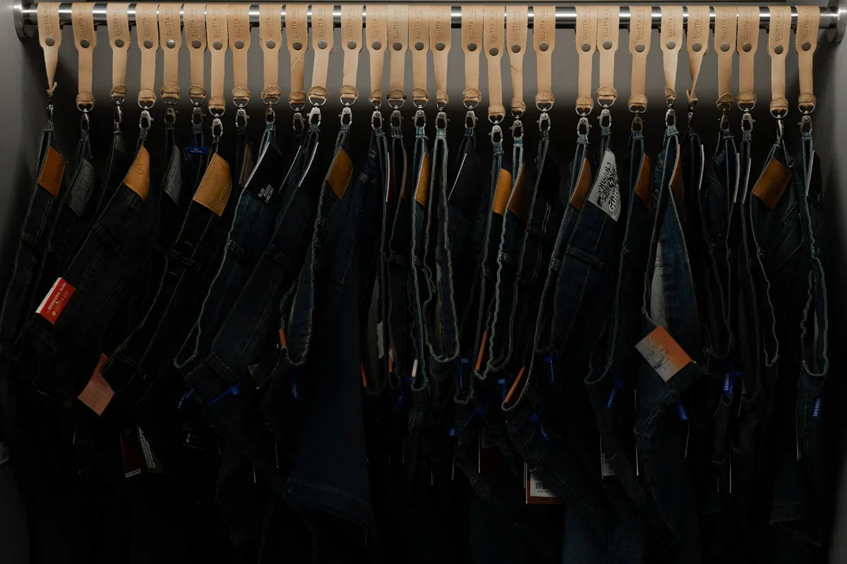 Flera par jeans hänger på rad i butik, ordnade med läderremmar, mode för nördar