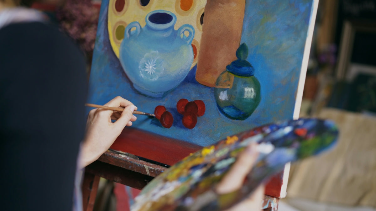 Artist painting a still life with blue vase and fruit