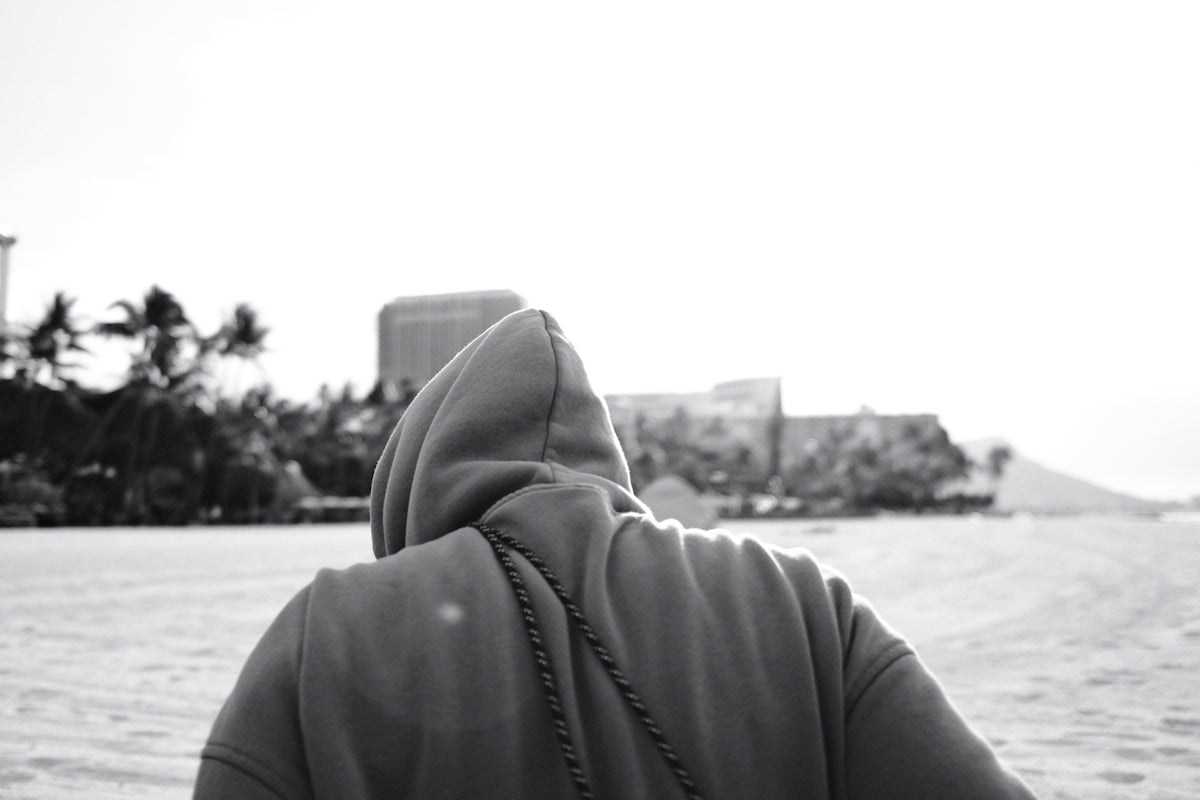 Person in hoodie facing away on a sandy beach.